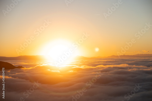 Above the clouds at sundown with a big brilliant sun in the center