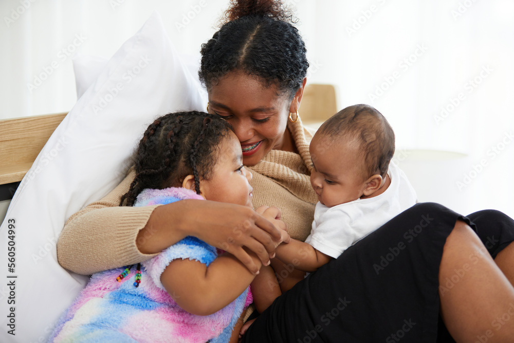 African young mother with her infant baby and kid smiling and hugging on bed