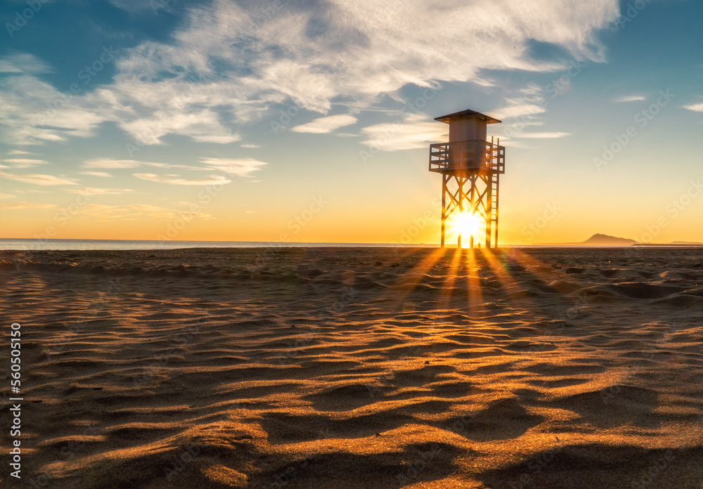 The sun behind the lifeguard post on the empty beach at sunrise