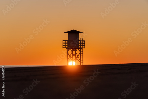 The sun behind the lifeguard post on the empty beach at sunrise © MiguelAngel