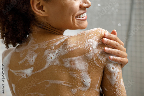 Fotografia, Obraz Close up of smiling african woman taking a shower with gel or shampoo foam in ba