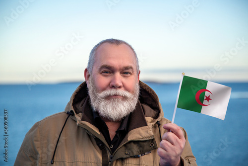 Man holding Algeria flag. Portrait of older man with a national Algerian flag. Visit Algeria. Older man 50 55 60 years old with gray beard outdoors travelling in winter. Travel to Algeria.