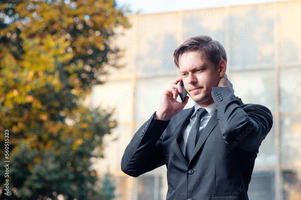 Bad news. Worried young businessman in suit and tie talking on the mobile phone while standing outdoors with office building in the background Bad news. Worried young businessman in suit and tie talking on the mobile phone while standing outdoors with office building in the background