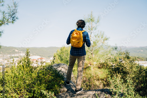 Man hiker with yellow backpack standing on the mountain rock. A tourist stands against the background of a valley. Rearview of a male hiker standing alone on a hill.