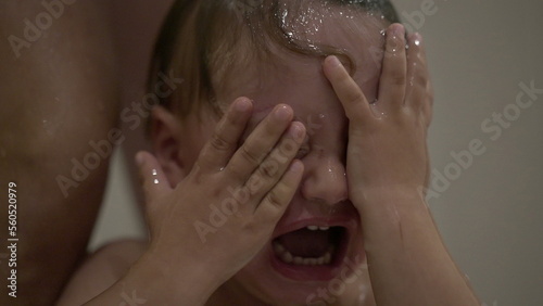 Upset baby washing hair. Crying toddler rubbing eyes and face