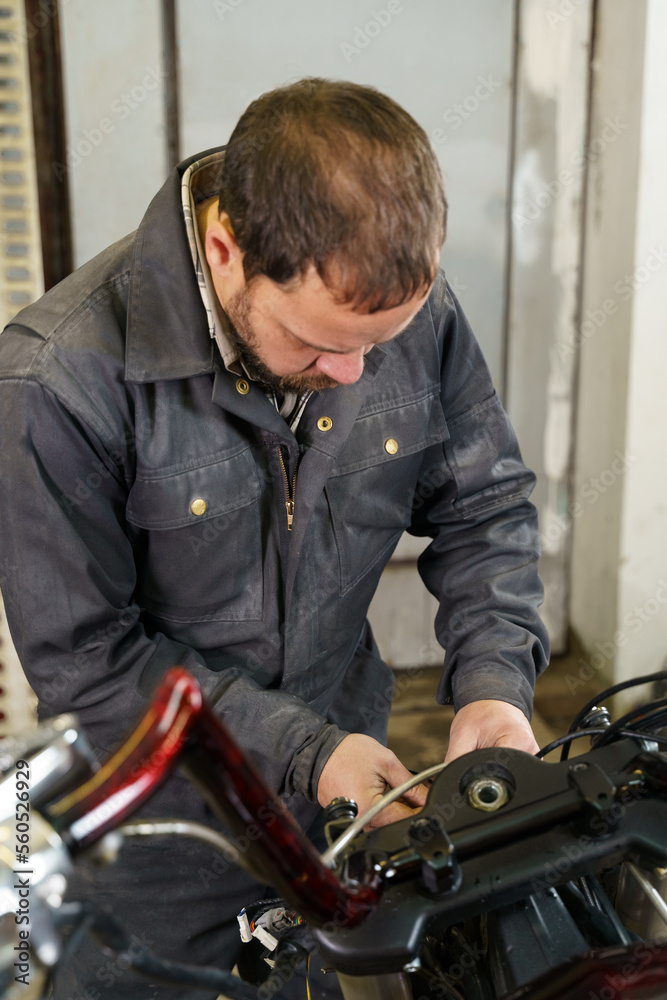The mechanic connects the electrical cables of the motorcycle. Vertical frame.