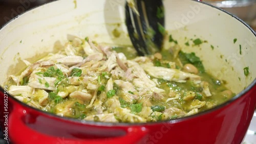 Spoon stirring chicken in dutch oven pot steaming