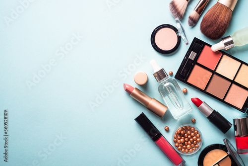 Make up professional cosmetics on blue background. Powder, lipstick, shadow, brushes with green leaves. Flat lay with copy space.
