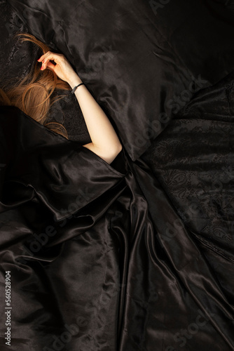 Female red hair and a hand on black bed sheet. Sleeping concept.