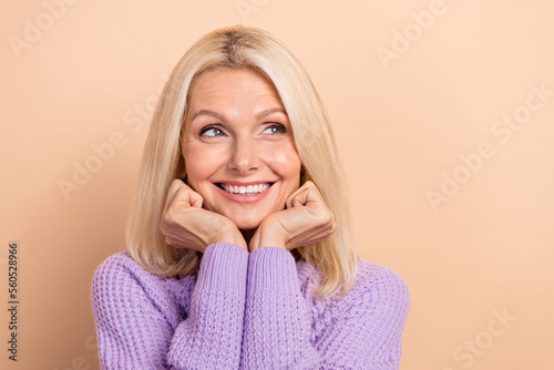 Portrait of adorable lovely person beaming smile hands touch cheeks look empty space isolated on beige color background