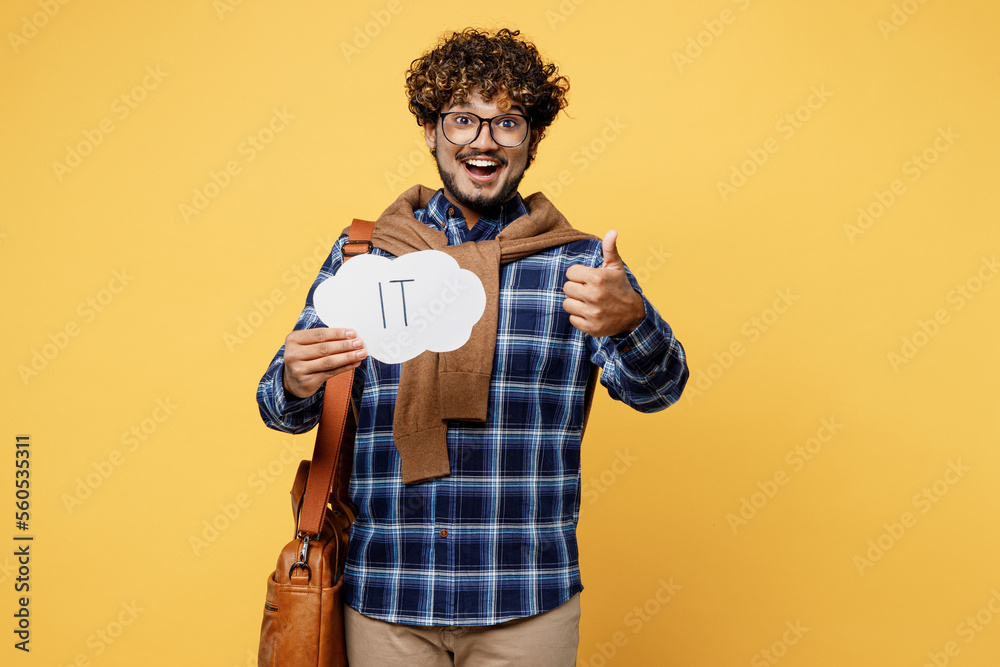 Full body young teen Indian boy student he wears casual clothes shirt glasses bag hold card sign with IT title text choose proffession isolated on plain yellow color background. University concept. Full body young teen Indian boy student he wears casual clothes shirt glasses bag hold card sign with IT title text choose proffession isolated on plain yellow color background. University concept.