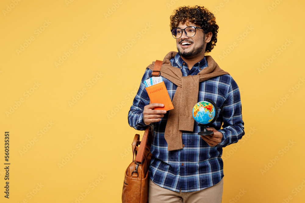 Traveler Indian boy IT student wear casual clothes hold passport ticket globe Earth map look aside isolated on yellow background Tourist travel abroad to study at university Air flight trip concept. Traveler Indian boy IT student wear casual clothes hold passport ticket globe Earth map look aside isolated on yellow background Tourist travel abroad to study at university Air flight trip concept.