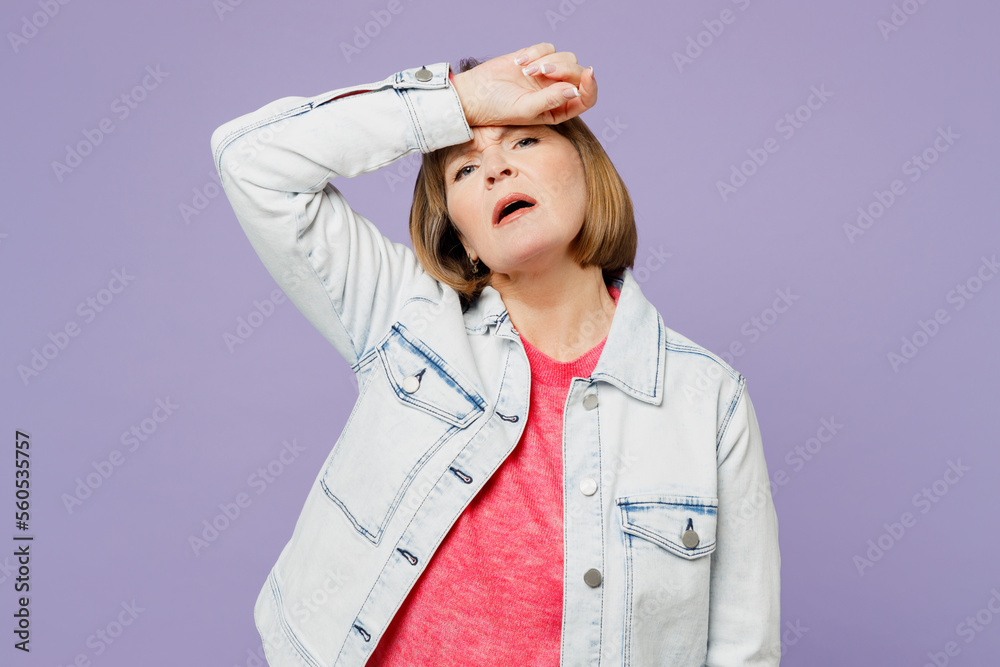 Elderly sick ill sad blonde woman 50s years old she wear casual clothes denim jacket t-shirt put hand on forehead suffer from headache isolated on plain pastel light purple background studio portrait. Elderly sick ill sad blonde woman 50s years old she wear casual clothes denim jacket t-shirt put hand on forehead suffer from headache isolated on plain pastel light purple background studio portrait.