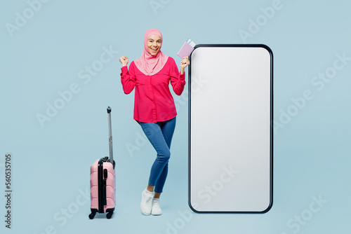 Foto Traveler arabian muslim woman wear pink abaya hijab big huge blank screen area mobile cell phone isolated on plain blue background Tourist travel abroad rest getaway Air flight trip free time concept