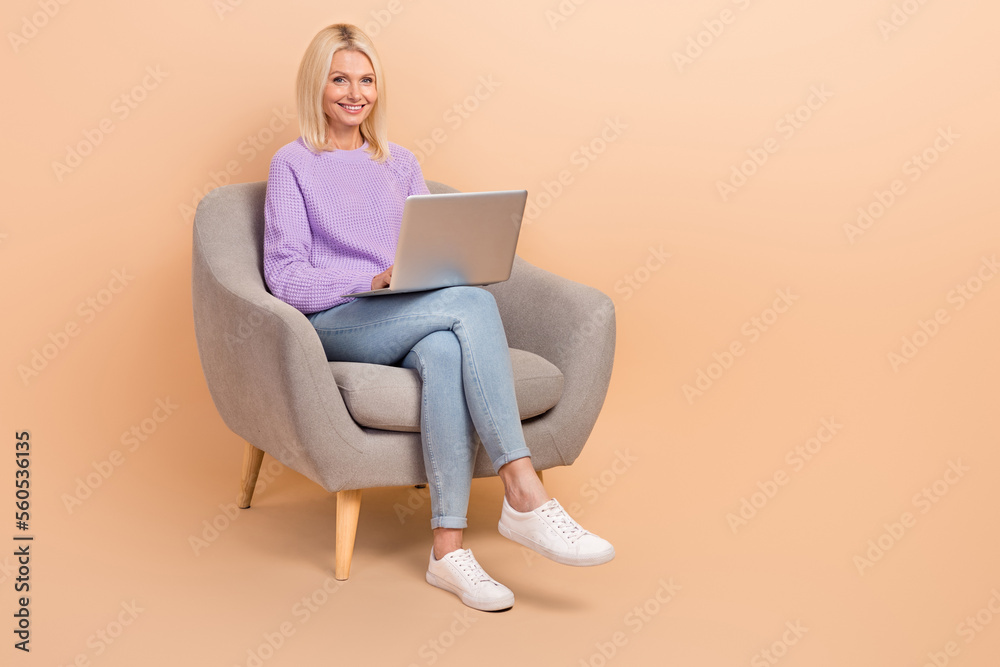 Full length photo of smart woman wear knit sweater jeans sit on armchair writing email remote job isolated on beige color background Full length photo of smart woman wear knit sweater jeans sit on armchair writing email remote job isolated on beige color background