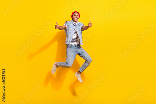 Full length photo of cool cheerful guy dressed denim clothes jumping high showing thumbs up isolated yellow color background © deagreez