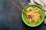 Asian noodles soup in green rustic ceramic bowl with wooden chopsticks top view on rustic stone background. Lo mein noodles with bouillon and green onion, space for text