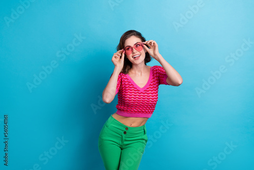 Photo of gorgeous pretty girl with curly hairdo dressed pink top hands touch sunglass look empty space isolated on blue color background