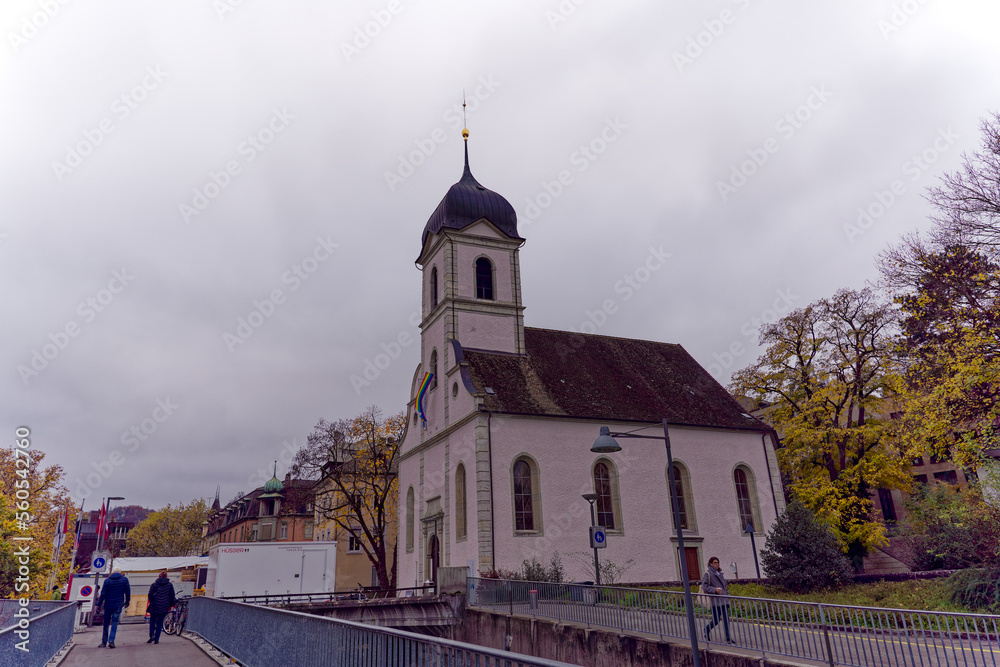 Entrance of catholic church with rainbow LBGT flag at City of Baden, Canton Aargau, on a cloudy gray autumn day. Photo taken November 13th, 2022, Baden, Switzerland.