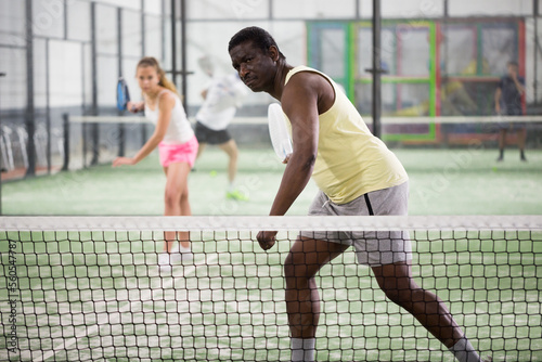 Sporty afro american man in yellow t-shirt playing padel tennis indoor