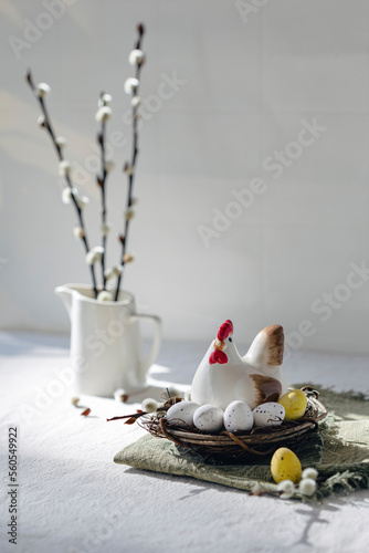 Ceramic chicken in a nest with colorful chocolate eggs on a light background
