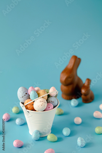 Colorful chocolate eggs in a white bucket on a blue background