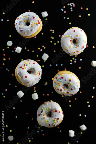 Donuts, marshmallows and cake sprinkling on a black background, levitation