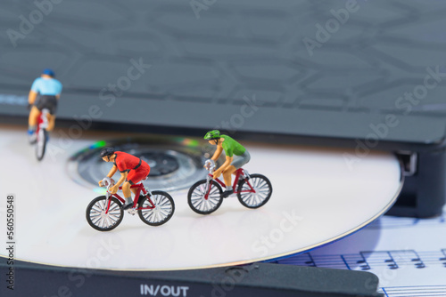 several cyclists ride on a white cd in a cd player lying on a sheet of music. closeup from above