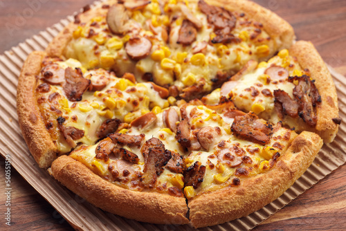 Freshly baked american pan pizza with a lot of cheese  chicken sausage  thin and crispy kebab meat and corn on a wooden board  take-away dish