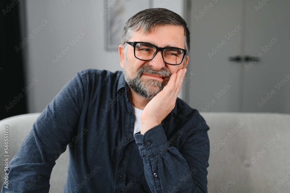 Elderly Man Having Toothache Touching Cheek Suffering From Pain Sitting On Sofa At Home. Selective Focus Elderly Man Having Toothache Touching Cheek Suffering From Pain Sitting On Sofa At Home. Selective Focus