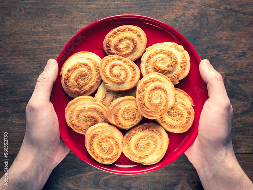 Deliciously crisp flaky cookies in the shape of a spiral on a red plate in human hands. Homemade Arlette Biscuits, top view photo