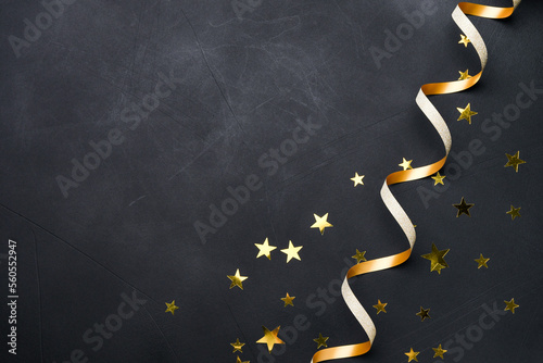 Festive black background holiday decorations golden shiny confetti in the form of stars and gold ribbon spiral serpentine on black background. Copy space