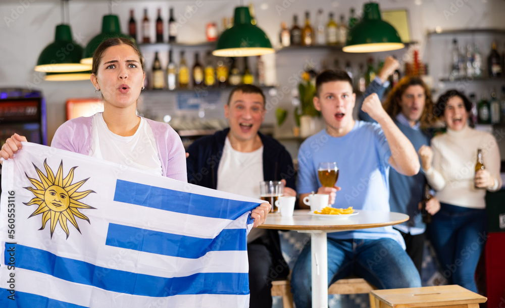 Obraz premium Fans with the flag of Uruguay celebrate the victory of their favorite team in a beer bar