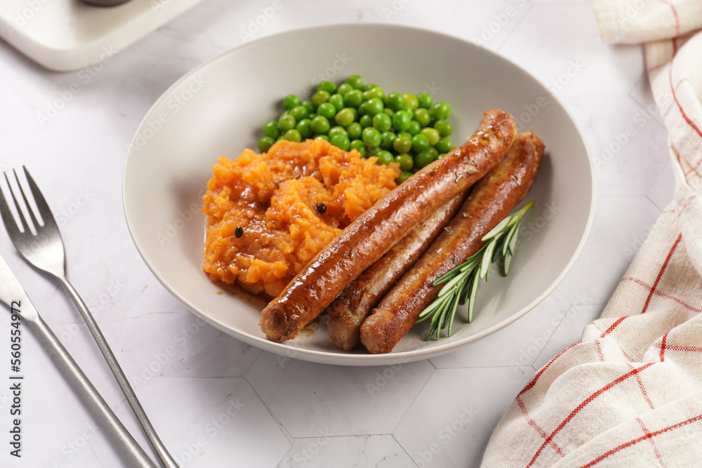 A lunch dish - boiled mashed sweet potato, steamed green peas and pork roasted sausages in a light grey bowl on a marble background A lunch dish - boiled mashed sweet potato, steamed green peas and pork roasted sausages in a light grey bowl on a marble background