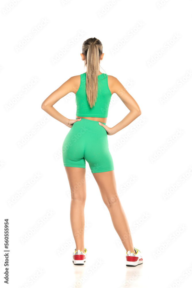 young sporty woman in green shorts and top posing on white background. Back view