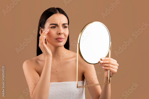 Stressed half-naked woman looking at mirror and touching her face