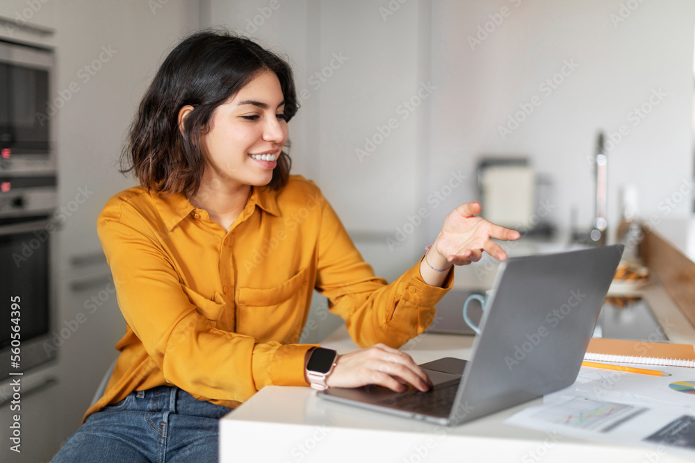 Smiling Young Arab Woman Making Video Call With Laptop In Kitchen Smiling Young Arab Woman Making Video Call With Laptop In Kitchen