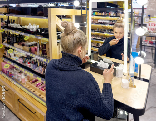 Woman buying make up at cosmetics section in store. choosing cosmetics, perfumes, creams and shampoos, Using tester.