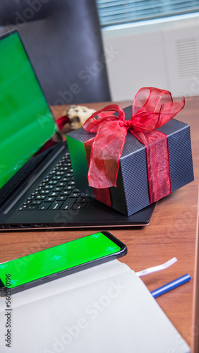 Laptop mock up grrn blank screen with gift box and phone with green screen on office desk. Valentine's day gift, love, heart, online shopping. photo