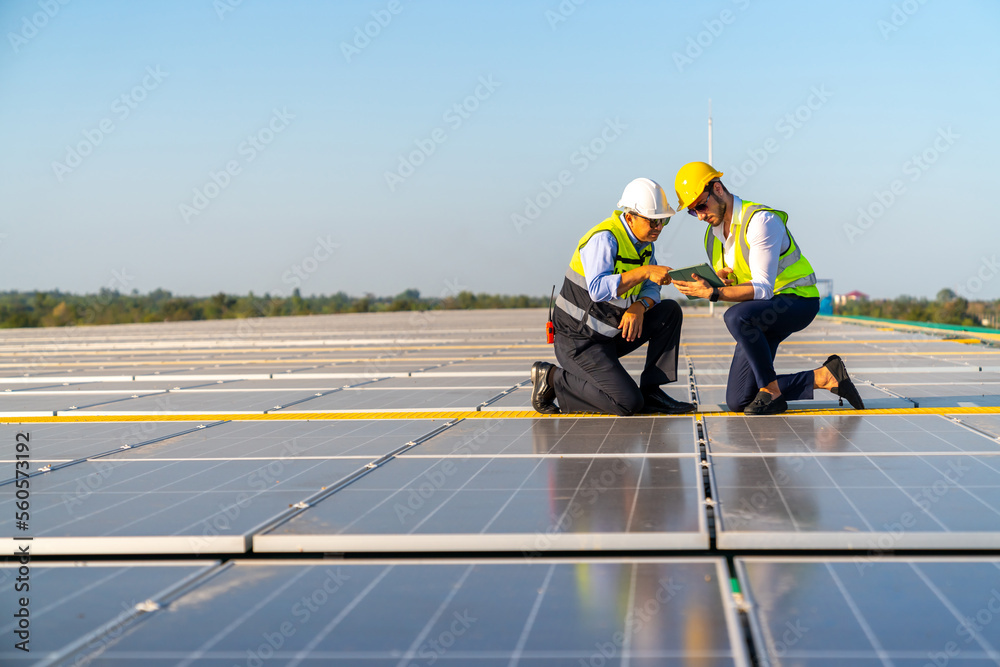 Fototapeta premium Professional man engineer using digital tablet maintaining solar cell panels together on building rooftop. Technician team working on ecological solar farm. Renewable clean energy industry concept.
