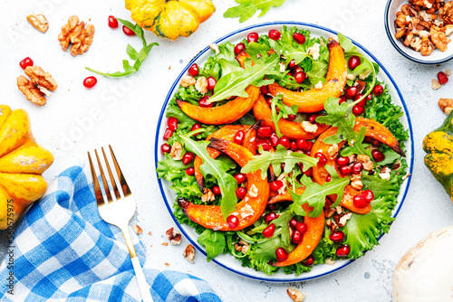 Fresh pumpkin salad with baked sweet pumpkin, lettuce, arugula, pomegranate and nuts. Healthy vegan comfort food. White background. Top view