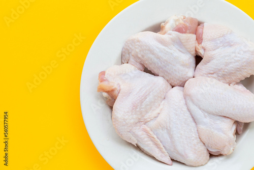 Fresh raw chicken wings in white plate on yellow background.