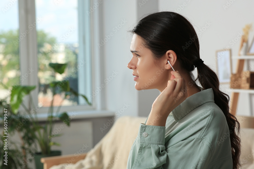 Young woman cleaning ear with cotton swab at home, space for text Young woman cleaning ear with cotton swab at home, space for text