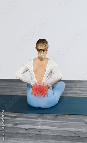 Back pain during yoga. A young woman rear view sits on a yoga mat and holding onto her sore back. (ID: 560587936)