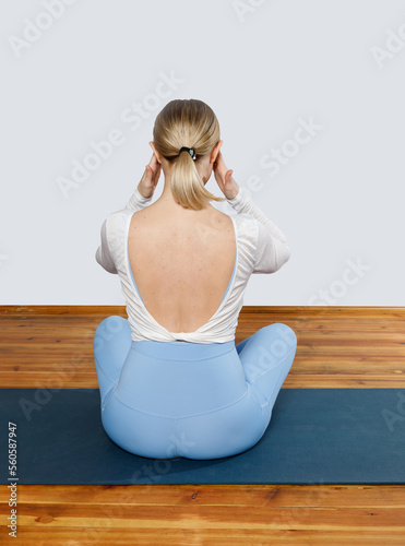 Head pain during yoga. A young woman rear view sits on a yoga mat and holding her sore head. (ID: 560587947)