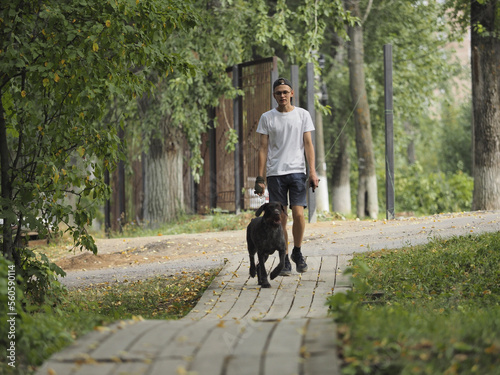 A young man of European appearance walks his dog in the park in the summer. © Ольга Кожина