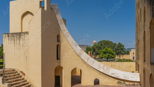 A fragment of the world's largest ancient sundial Samrat Yantra on a blue sky background. The walls, the sandstone staircase and the marble surface of the curved measuring scale are visible. photo
