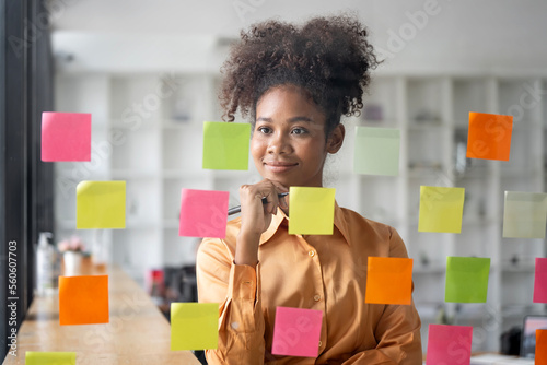 Papier peint Young smiley attractive, businesswoman using sticky notes in glass wall to writi