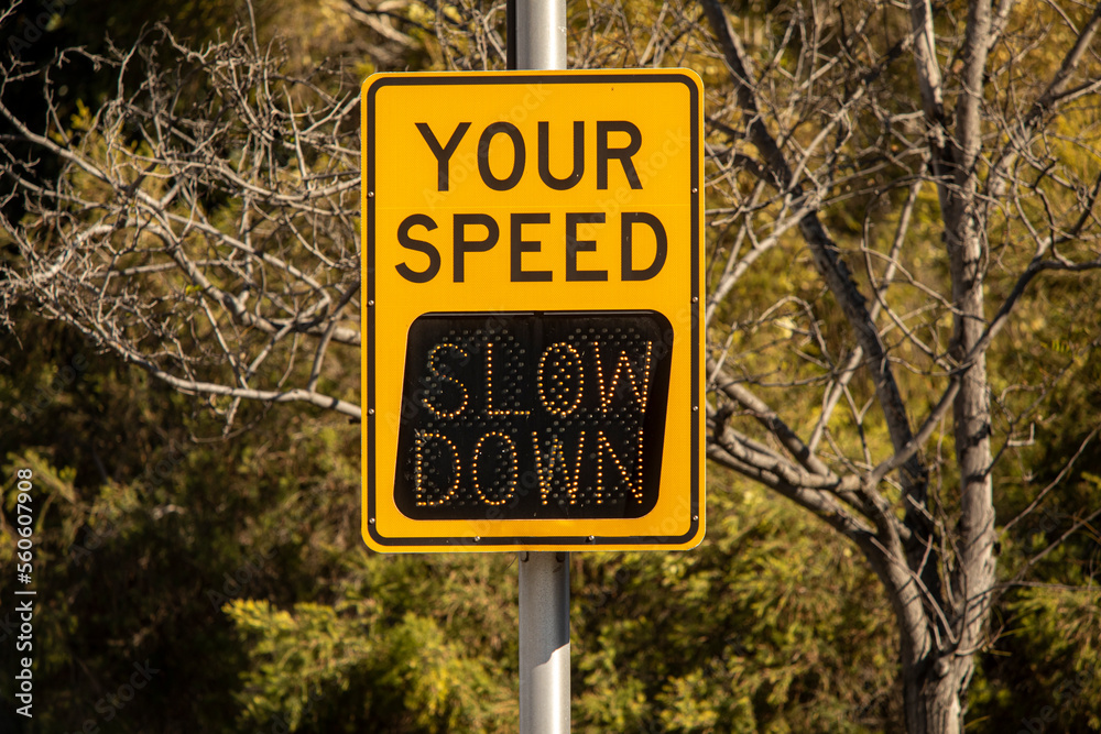Yellow digital sign measuring traffic speed. The sign says Your Speed  and shows Slow Down in digital letters
