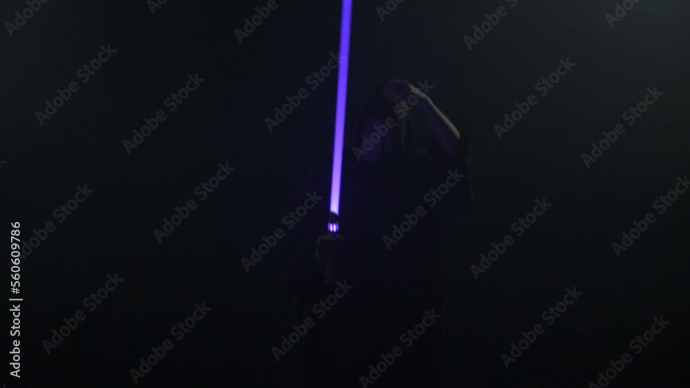 Young man in Jedi cosplay costume with lightsaber battle on black background in smoke and rain, 4k slow motion video filmed on 8k camera nikon z9